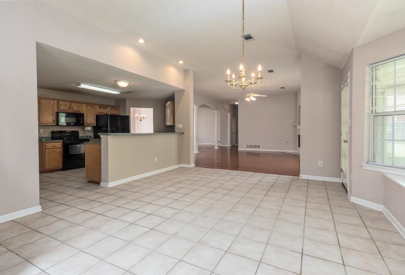 Kitchen and dining area featuring tile flooring, wood cabinetry, black appliances, a breakfast bar, and vaulted ceilings
