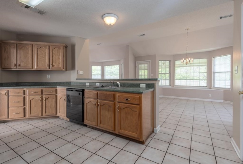 Kitchen featuring tile flooring, wood cabinetry, dark countertops, and a built-in dishwasher