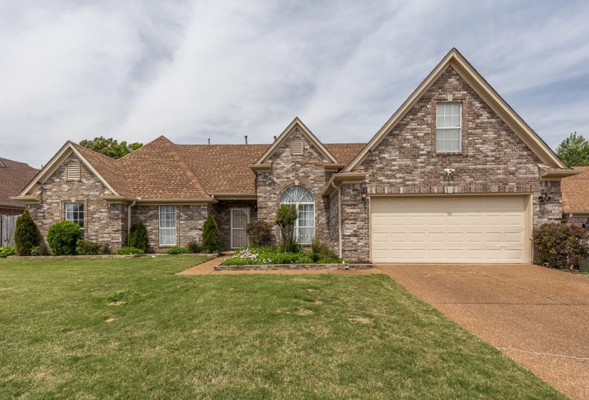 Brick exterior residence featuring a prominent two-car garage, pitched rooflines, and a landscaped front yard with a stone-edged flower bed