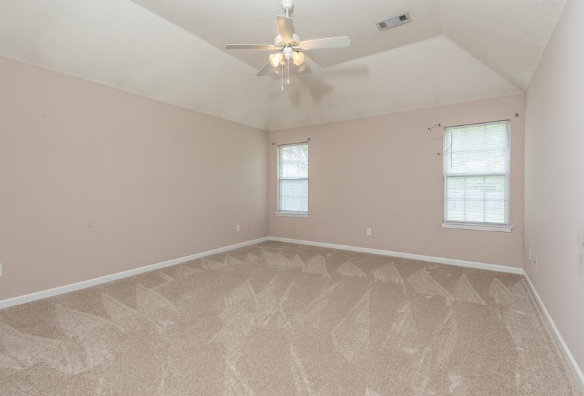 Spacious room featuring vaulted ceilings, light neutral wall paint, two windows, and a ceiling fan