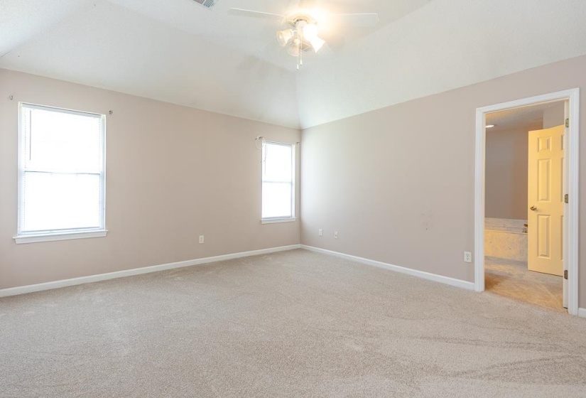 Spacious room featuring vaulted ceilings, two large windows, neutral-toned walls, and a ceiling fan