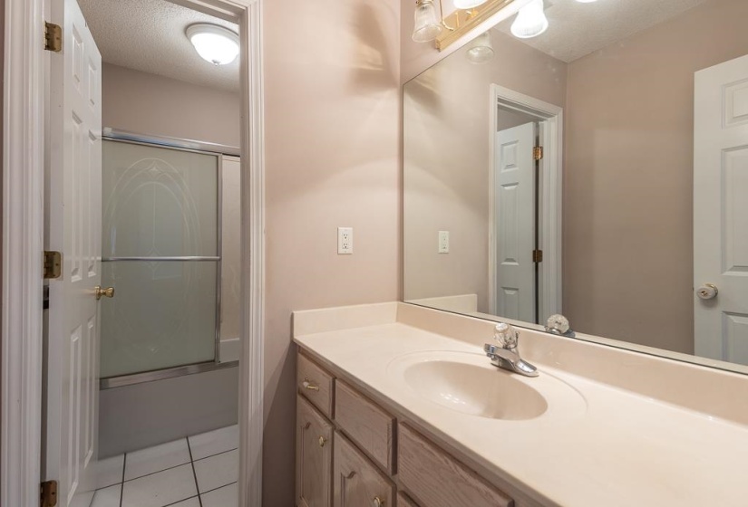 Bathroom featuring a single vanity with an integrated sink, a large wall-mounted mirror, and a tub/shower combination with sliding frosted glass doors