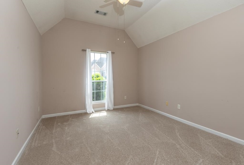 Room featuring vaulted ceilings, a central window with exterior surroundings visible, and a ceiling fan with light fixture