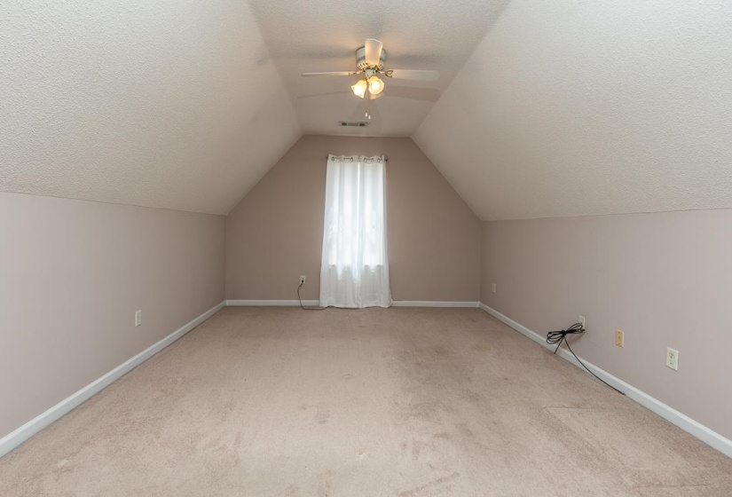 Carpeted room with a vaulted ceiling, a centered window with white curtains, and a ceiling fan with integrated lighting