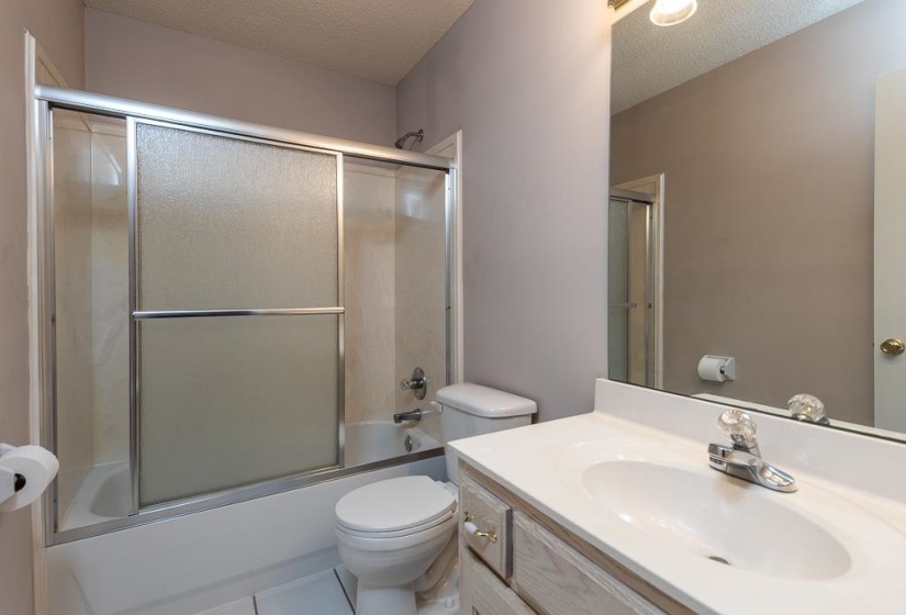 Bathroom featuring a white vanity with an integrated sink, a large wall-mounted mirror, and a tub/shower combination with sliding frosted glass doors