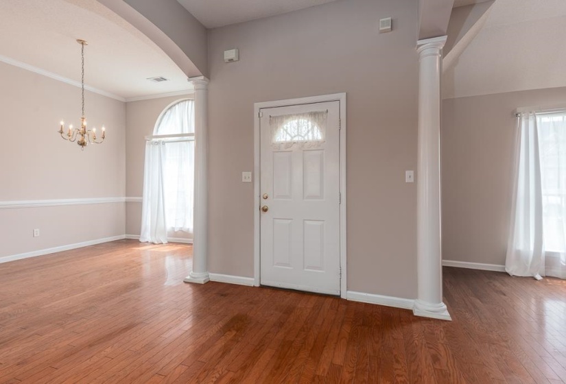 Entryway with hardwood flooring, a paneled front door featuring a transom window, and architectural columns