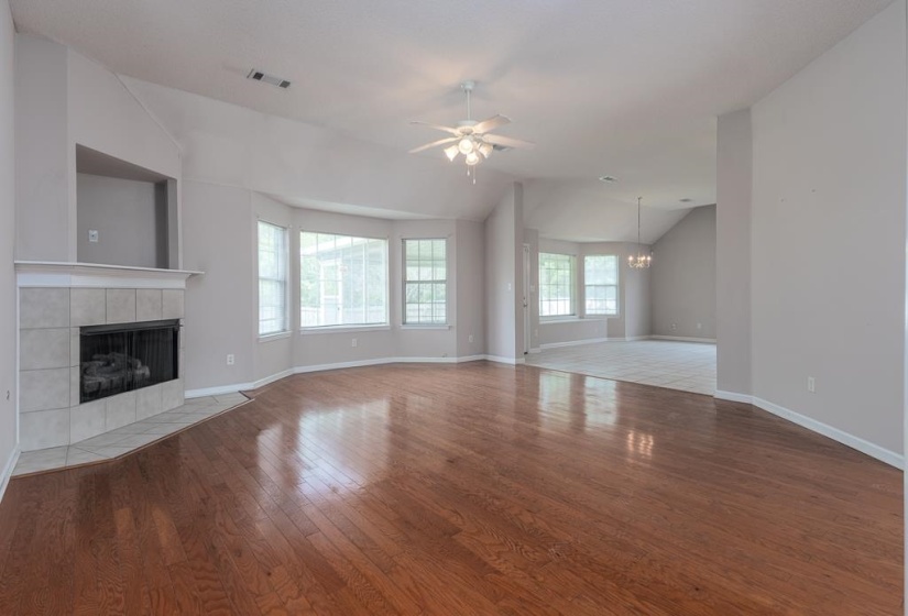 Spacious living area featuring wood-finish flooring, a tiled fireplace with mantel, vaulted ceilings, and a ceiling fan