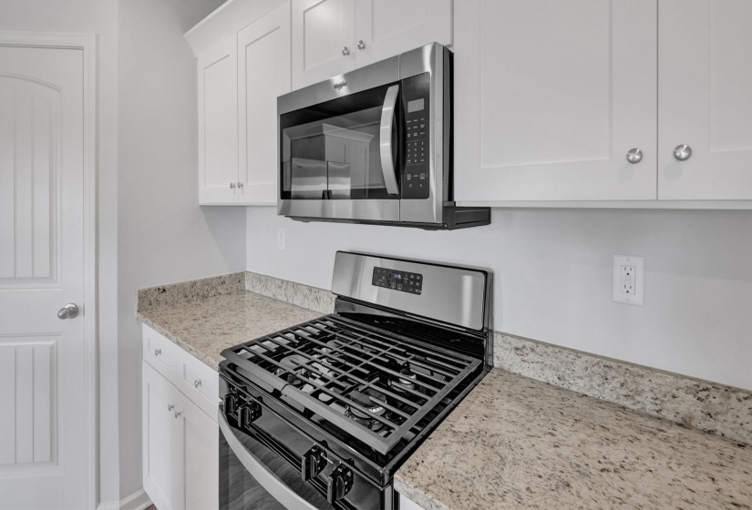 Kitchen featuring a stainless steel gas range, coordinating microwave, white upper and lower cabinetry, and light-toned speckled countertops