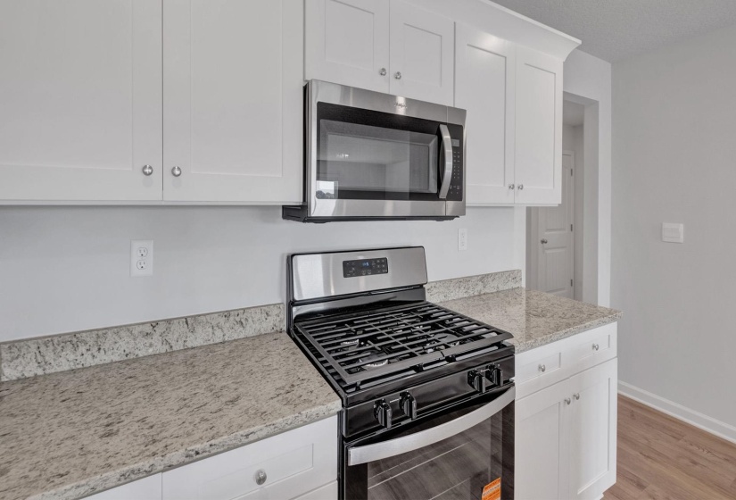 Kitchen featuring white shaker-style cabinetry with crown molding, stainless steel gas range, stainless steel microwave, and speckled countertops