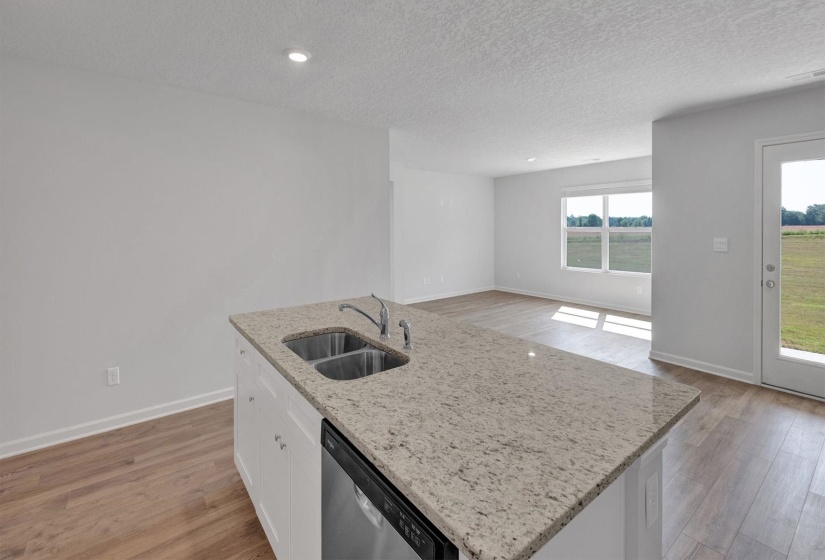 Kitchen island featuring a dual basin sink with a chrome faucet, light-toned countertop, and integrated dishwasher