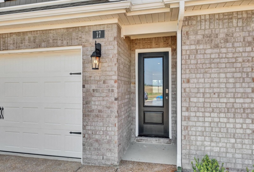 Brick exterior featuring a white paneled garage door with decorative hardware, a black front door with an upper glass panel, a prominent exterior lantern light fixture, and a clearly visible house number