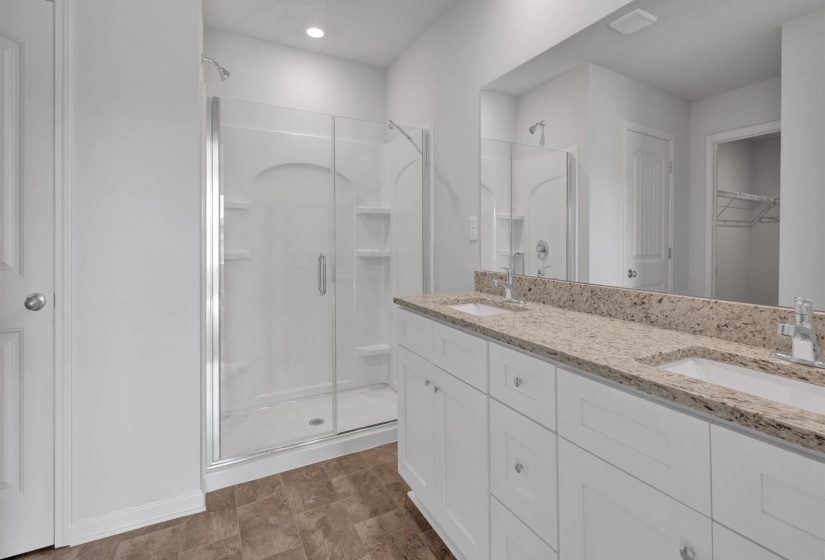 Spacious bathroom featuring a double vanity with stone-finish countertop, dual undermount sinks, and white shaker-style cabinetry