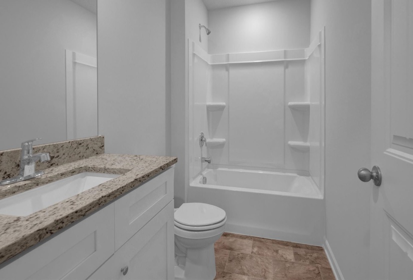 Bathroom featuring a granite-look countertop vanity with integrated sink, white cabinetry, chrome faucet, and a white bathtub with shower surround