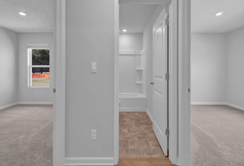 Centrally positioned bathroom featuring a tub/shower combination with integrated shelving, brown-toned tile-finish flooring, and a white paneled door