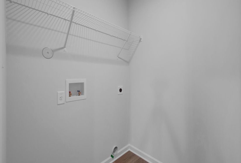 Dedicated laundry area featuring a white wire shelving unit, integrated washer hookups, and wood-finish flooring