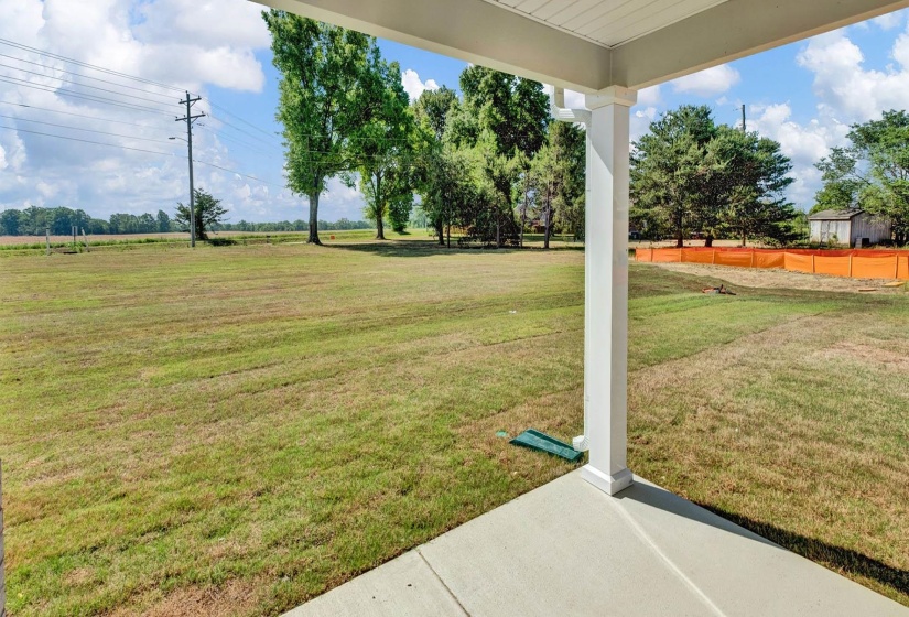 Concrete patio with a white support column and ceiling, overlooking a large grassy area with mature trees