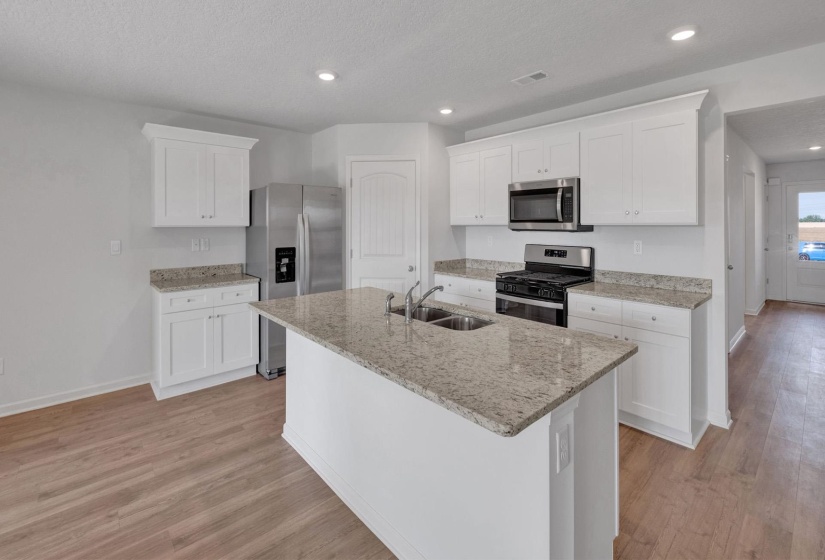 Open-concept kitchen featuring an island with double sink, white cabinetry, granite countertops, stainless steel appliances, and wood-finish flooring