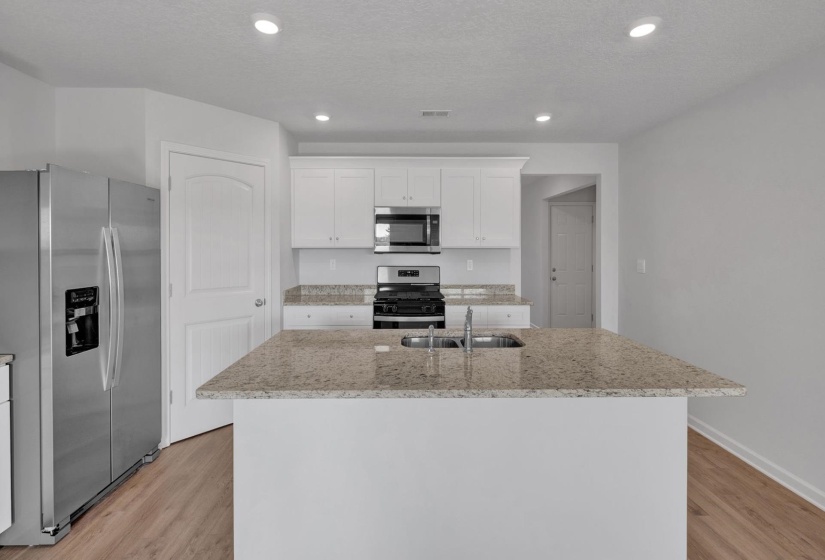 Kitchen featuring a central island with an undermount sink, granite-style countertops, white cabinetry, stainless steel appliances, and wood-finish flooring