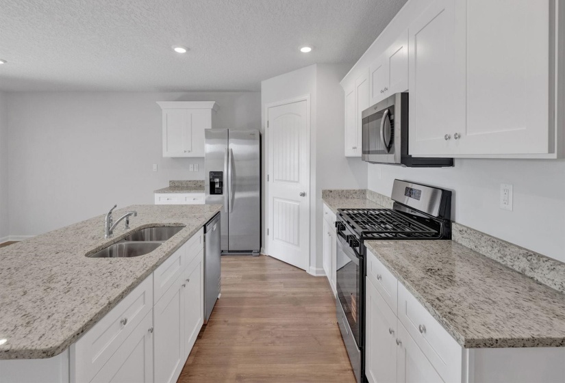 Modern kitchen featuring white shaker cabinetry, stainless steel appliances, speckled stone countertops, a double basin sink, and wood-finish flooring