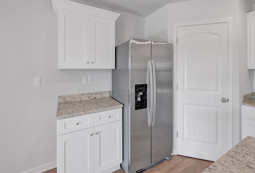 Stainless steel side-by-side refrigerator, white shaker-style cabinetry, light-toned granite-style countertops, wood-finish flooring, and a white paneled door