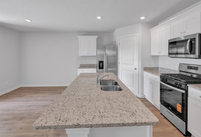 Kitchen featuring a spacious island with an integrated double basin sink, light-toned countertops, white cabinetry, stainless steel appliances, and recessed lighting