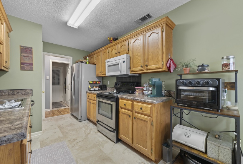 Kitchen featuring light wood cabinetry, stainless steel appliances, stone-finish countertops, and neutral tile flooring