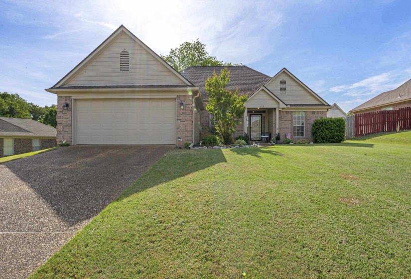 Exterior featuring a two-car garage, stone and siding facade, covered entry, and a sloped, grassy front yard