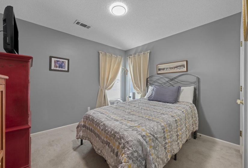 Bedroom featuring neutral gray walls, light carpet flooring, a window with blinds and drapes, and a flush-mount ceiling light