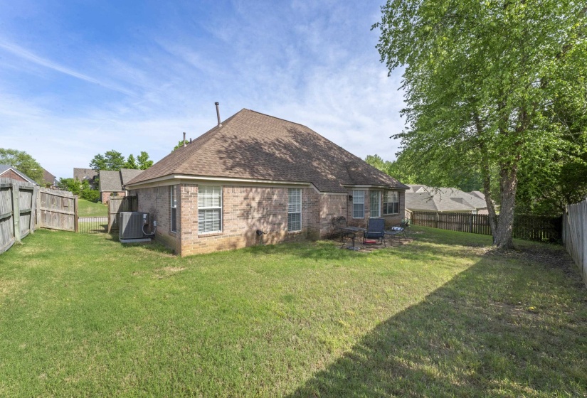 Spacious backyard featuring a manicured lawn, established mature trees, a brick exterior, and a privacy fence