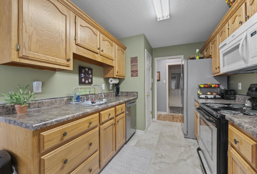 Galley kitchen featuring light wood cabinetry, laminate countertops, a stainless steel sink with a gooseneck faucet, and a tile-look flooring