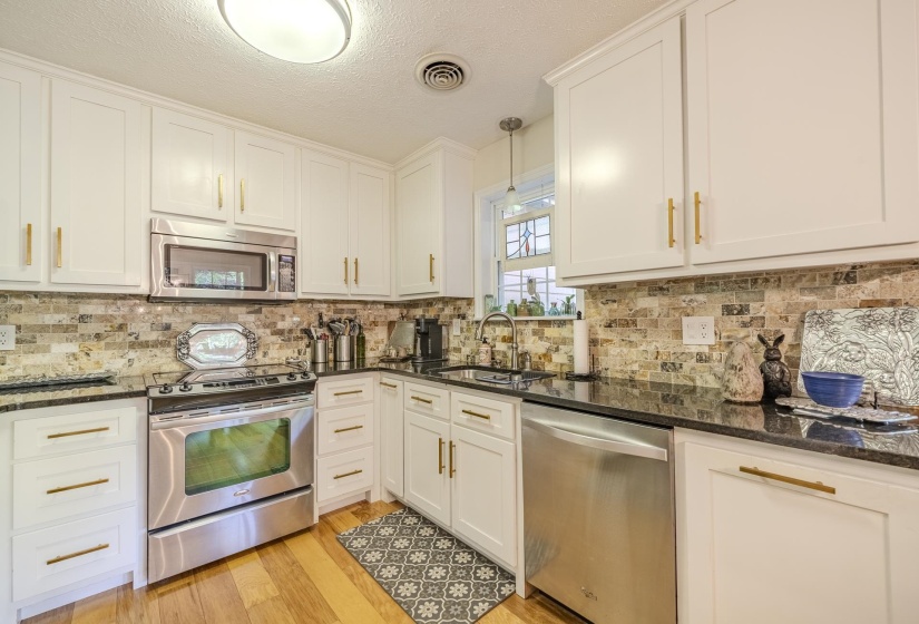 Kitchen featuring white cabinetry with gold-finish hardware, stainless steel appliances, black countertops, and a patterned tile backsplash