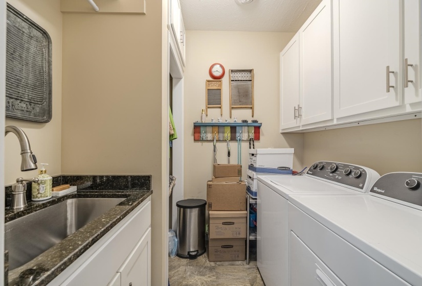 Dedicated utility room featuring white cabinetry, a stainless steel sink with a dark speckled countertop, and durable flooring