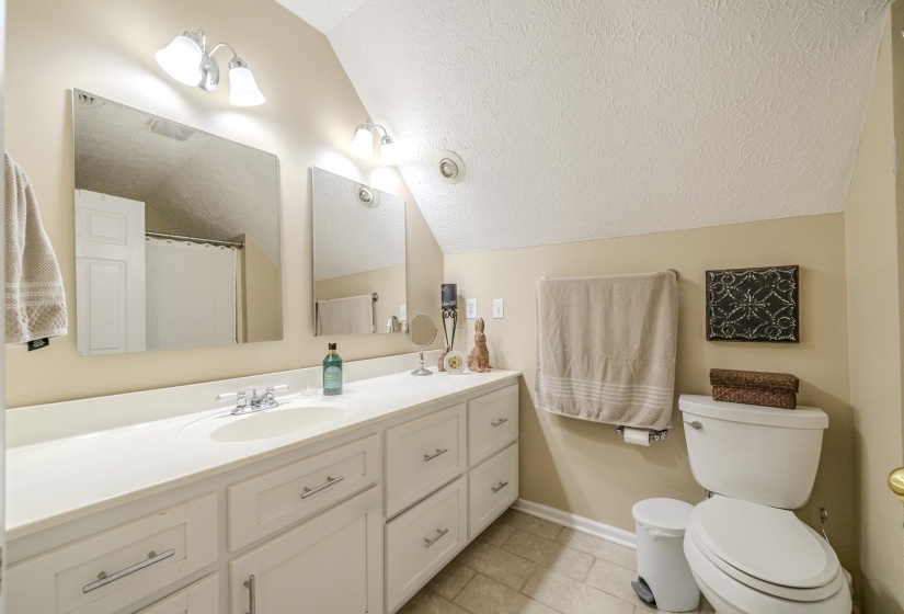 Bathroom featuring a double vanity with integrated sinks, white cabinetry with silver hardware, two wall-mounted mirrors, and an angled ceiling