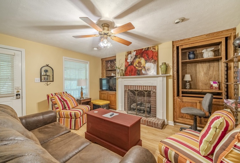 Living area featuring a brick fireplace with a white mantel, wood-finish flooring, and built-in wood shelving