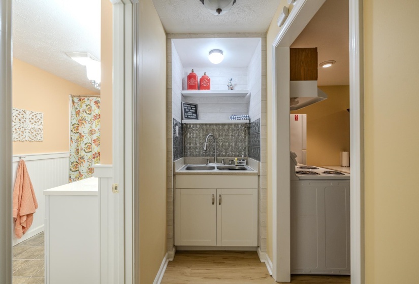 Compact utility area featuring a double basin sink, white cabinetry, decorative backsplash, and wood-finish flooring