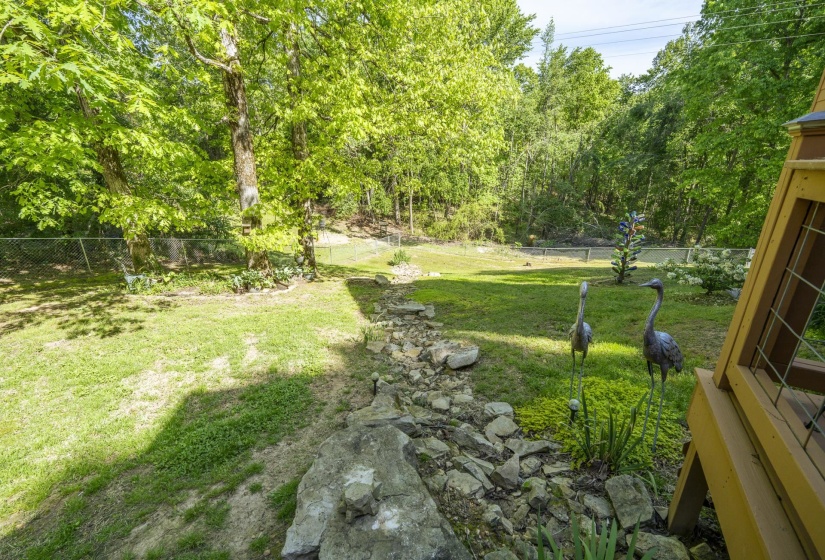 Expansive rear yard featuring a manicured lawn, established landscaping, mature trees, and a rock-lined dry creek bed