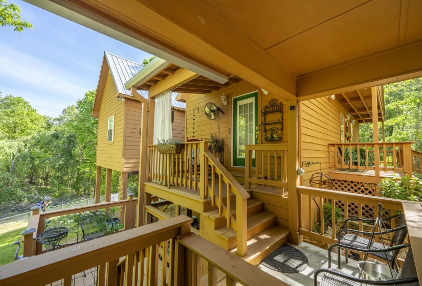 Multi-level outdoor living space featuring warm-toned wood construction, sturdy railings, a white metal roof, and a green painted exterior door