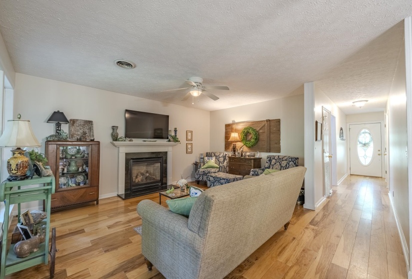 Spacious living area featuring wood-finish flooring, a fireplace with a white mantel, and a ceiling fan