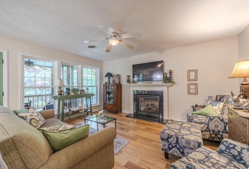 Spacious living area featuring wood-finish flooring, a ceiling fan, and a fireplace with a white mantel and dark surround