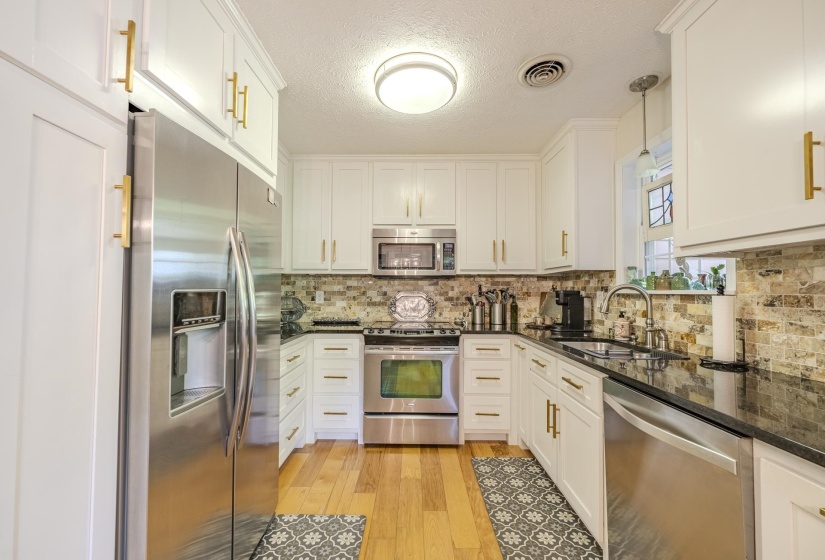 Kitchen featuring white shaker cabinetry with gold-tone hardware, black countertops, and a full suite of stainless steel appliances