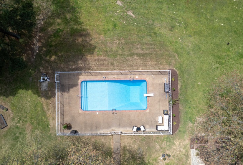 Rectangular swimming pool with concrete surround, featuring a diving board, integrated steps, and a perimeter fence