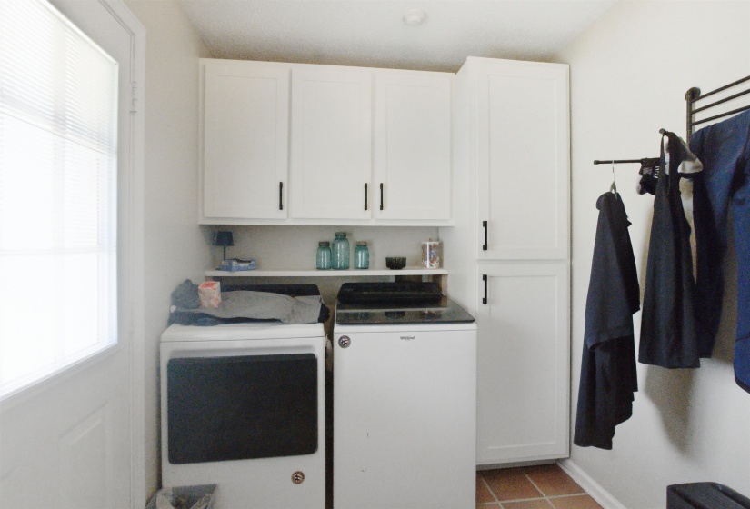 Utility space featuring white cabinetry with black hardware, open shelving, and terracotta-style floor tiles