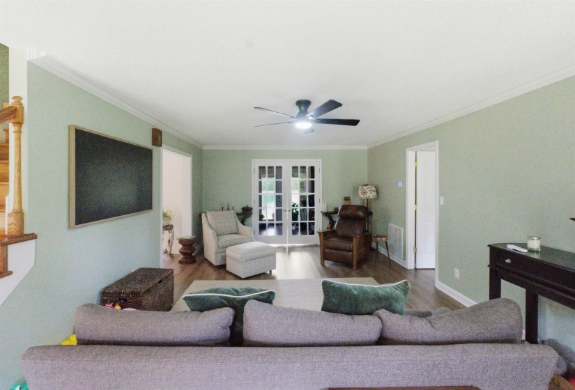 Spacious living area featuring wood-finish flooring, light green wall tones, and white crown molding