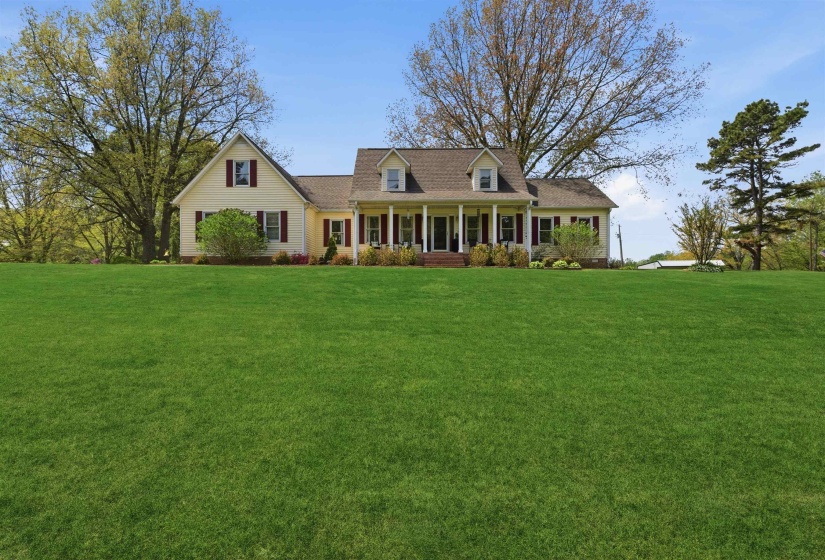 Expansive front lawn leading to a charming residence with a covered porch featuring white columns
