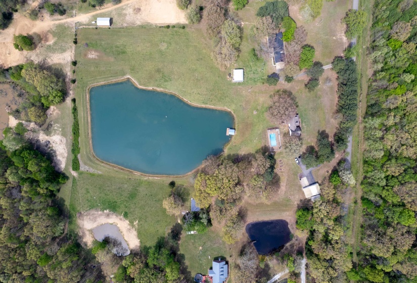 Expansive property featuring a large central pond with a dock, surrounded by lush green spaces and mature trees