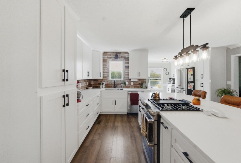 Spacious kitchen featuring an expansive island with a built-in gas range, white cabinetry, dark wood-finish flooring, a farmhouse sink, and a brick-finish backsplash