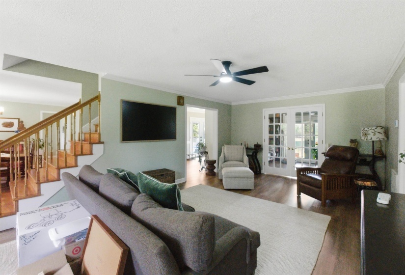 Spacious living area featuring wood-finish flooring, a ceiling fan, and crown molding