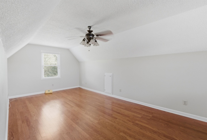 Spacious room with wood-finish flooring, a vaulted ceiling, and a ceiling fan with light fixture