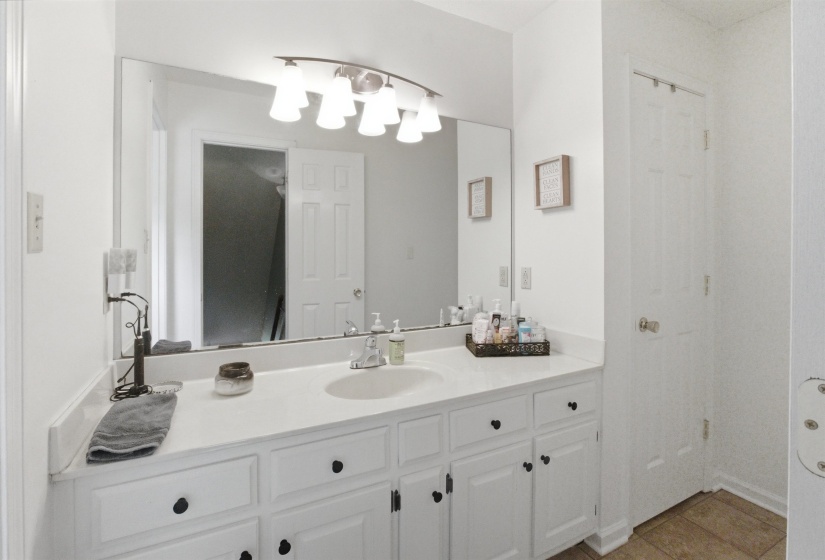 White vanity with a single basin sink, white countertop, and expansive mirror