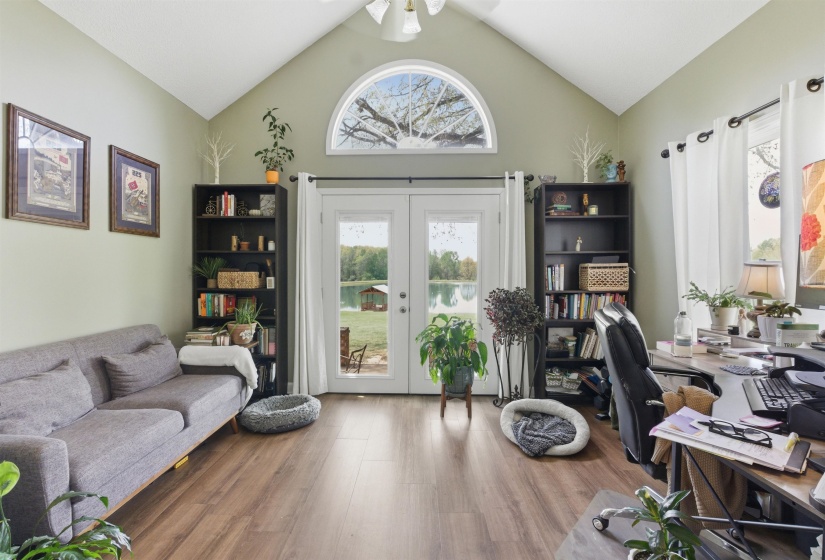 Vaulted ceiling room featuring French doors leading to a waterside setting, an arched transom window, wood-finish flooring, and two built-in shelving units